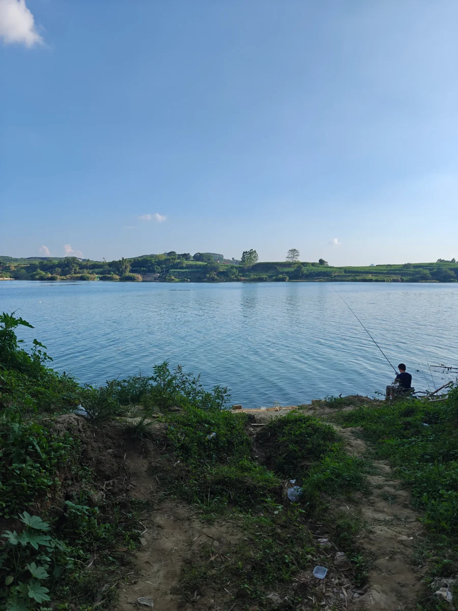蓝天、湖面、远岸树木与右下垂钓人物的原照片